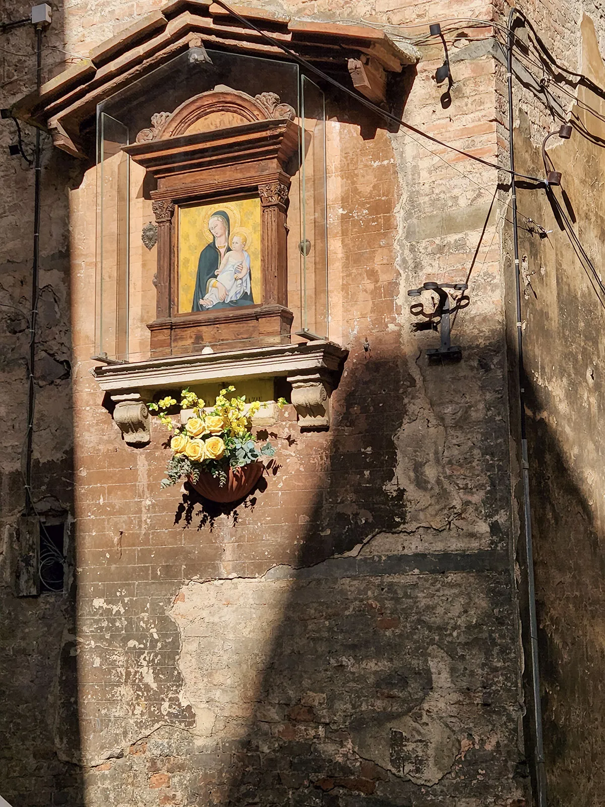 Tabernáculo de rua com Madonna e flores frescas — devoção popular que atravessa gerações